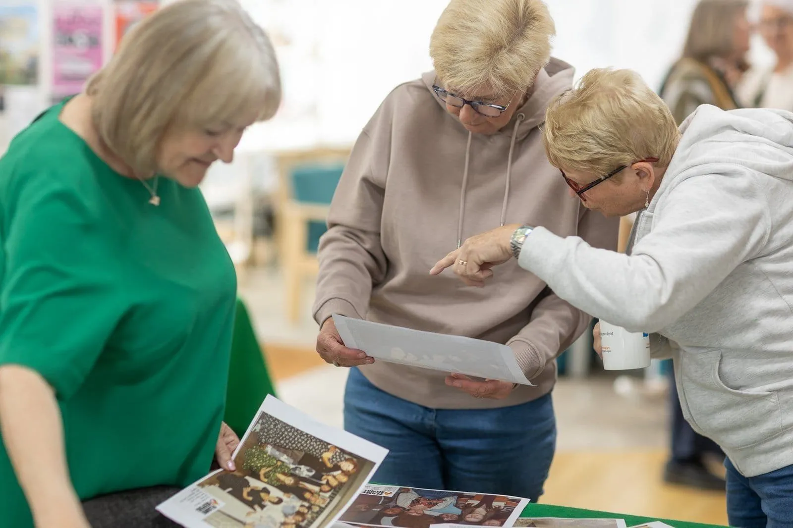 Three people lean over a table of printed photographs at the Ronson Reunited event, one holding a printed sheet and another pointing.