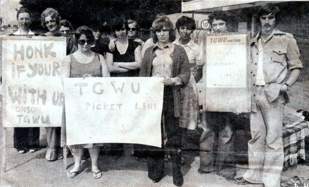 Black-and-white newspaper photograph of Ronson workers on a pavement during the strike, holding hand-painted TGWU picket line placards.