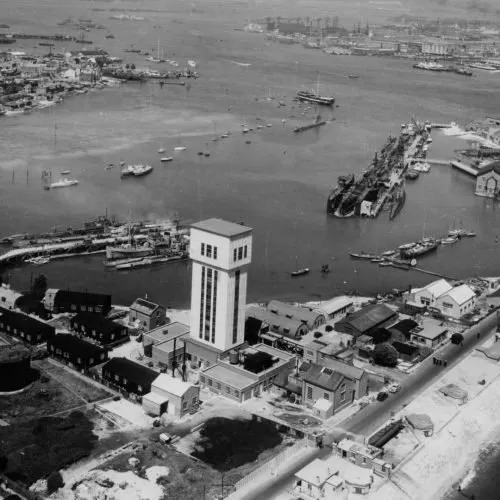 Black-and-white aerial photograph of Fort Blockhouse, with the submarine escape training tower in the foreground and Portsmouth Harbour beyond.
